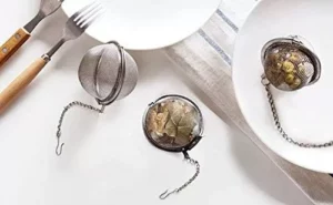 ثلاث منقوعات شاي معدنية مملوءة بأنواع مختلفة من بهارات الشاي موضوعة على أطباق بيضاء، مصحوبة بشوكة وملعقة.