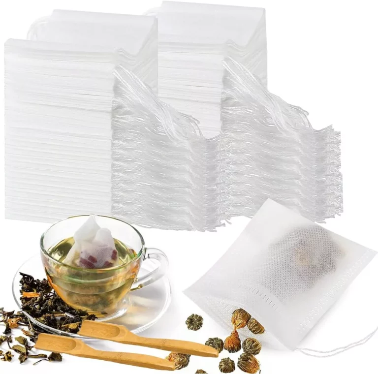 مجموعة من أكياس الشاي الفارغة مرتبة في أكوام مرتبة إلى جانب كوب زجاجي مملوء بالشاي، حيث تم غمر أحد أكياس الشاي بداخله. تنتشر حولها أنواع مختلفة من أوراق الشاي السائبة والعديد من المغارف الخشبية، مما يخلق مشهدًا جذابًا بصريًا مثاليًا لأي من محبي الشاي.