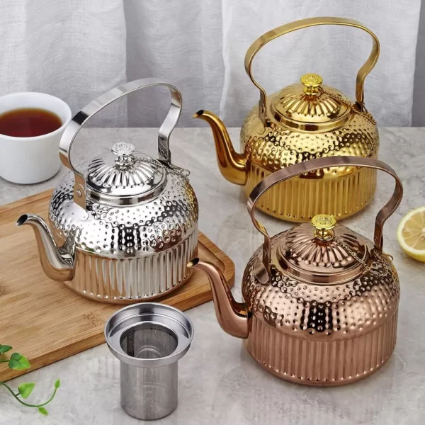 نص بديل: ثلاثة أباريق شاي معدنية باللون الفضي والذهبي والنحاسي على سطح رخامي بجانب كوب من الشاي وشريحة ليمون ومصفاة شاي.