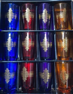 عرض جميل من أكواب زجاجية ملونة مزينة بأنماط ذهبية معقدة، مثالية للاستمتاع بأنواع مختلفة من الشاي. تعرض الصفوف مجموعة من الأكواب ذات الألوان الزرقاء والحمراء والأرجوانية والبرتقالية النابضة بالحياة.