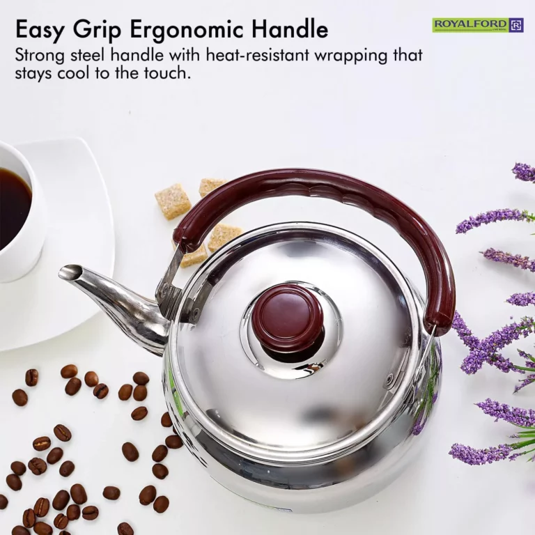 غلاية من الفولاذ المقاوم للصدأ بمقبض كستنائي اللون بجوار كوب أبيض من القهوة وحبوب القهوة المتناثرة على سطح أبيض نقي، مثالية لتحضير أنواع مختلفة من الشاي والشاي.