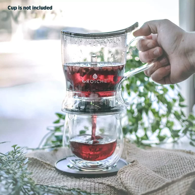 يد تسكب الشاي الأحمر في كوب زجاجي شفاف باستخدام مصفاة شاي زجاجية. الكوب غير متضمن في الصورة.