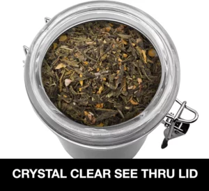 برطمان زجاجي يحتوي على أوراق شاي سائبة، مزود بغطاء شفاف. النص الموجود على البرطمان يقول "غطاء شفاف للغاية". مثالي لعرض أنواع مختلفة من الشاي وإضفاء لمسة أنيقة على مطبخك.