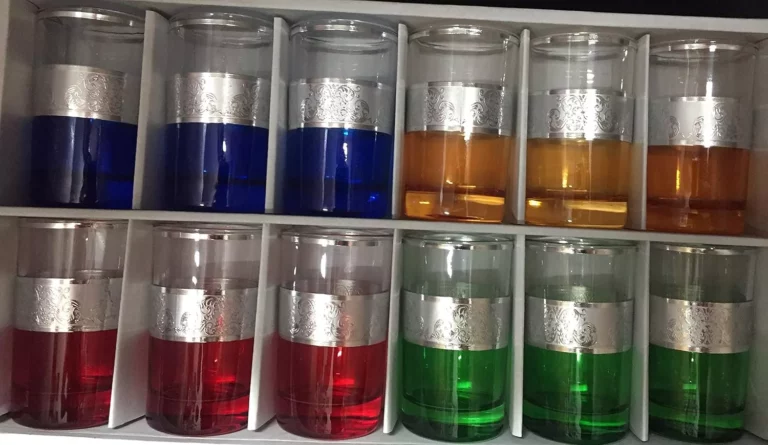 مجموعة رائعة من 12 كوب شاي بقواعد نابضة بالحياة باللون الأزرق والبرتقالي والأحمر والأخضر، مرتبة بشكل أنيق في صندوق أنيق مثالي لتقديم الشاي.