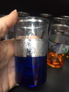 شخص يمسك كأسًا مزخرفًا ممتلئًا بنصف الشاي الأزرق؛ وتستحضر أكواب أنيقة مماثلة في الخلفية العرض المتطور لأنواع مختلفة من الشاي.