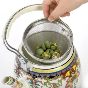 يد تحمل مصفاة شبكية مليئة بالمكسرات الخضراء فوق إبريق شاي مزخرف بنقوش زهرية نابضة بالحياة، استعدادًا للاستمتاع بالشاي التقليدي.