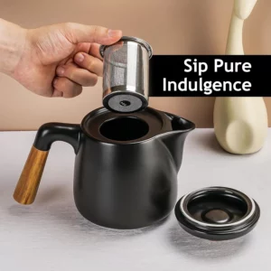 يد تحمل مصفاة شاي فوق إبريق شاي أسود أنيق بمقبض خشبي. النص المكتوب على الغلاف يقول "اشرب الانغماس الخالص". جرب أجود أنواع الشاي.