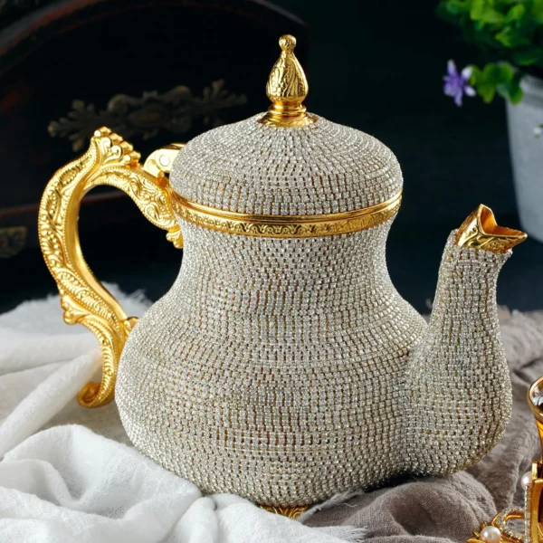 إبريق شاي مبهر مرصع بالجواهر مع مقبض ذهبي مصمم بشكل معقد وصنبور، موضوع بشكل أنيق على قطعة قماش بيضاء على خلفية داكنة، جاهز لتقديم أنواع مختلفة من الشاي لأصحاب الأذواق الراقية.