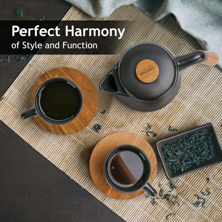 إبريق شاي أسود أنيق يتميز بلمسات خشبية، مصحوبًا بفنجانين شاي وطبق من أوراق الشاي السائبة، كل ذلك على حصيرة أنيقة من الخيزران. نص مكتوب عليه "انسجام مثالي".